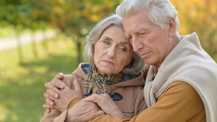 Ein älteres Paar umarmt sich liebevoll, es ist ein herbstlicher Park mit verschwommenem Hintergrund.